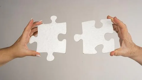 Two hands trying to connect puzzle piece on gray background. Teamwork concept Stock Photos