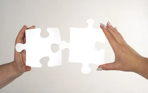Two hands trying to connect puzzle piece on gray background. Teamwork concept Stock Photos