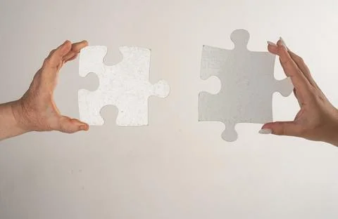 Two hands trying to connect puzzle piece on gray background. Teamwork concept Stock Photos