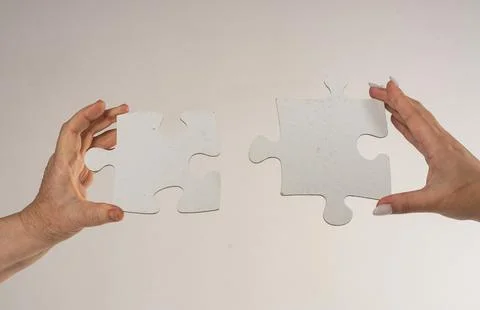 Two hands trying to connect puzzle piece on gray background. Teamwork concept 写真素材