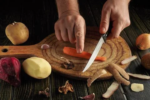 Two hands use a knife to cut a carrot on a wooden cutting board. Different ve Stock Photos
