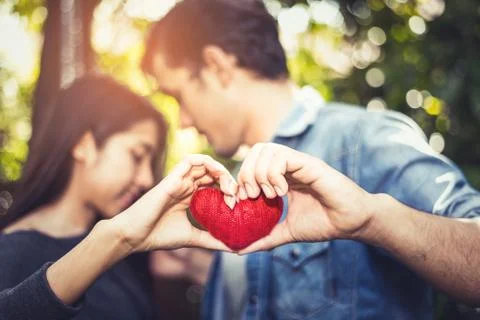 Two hands of young lovers or couple holding Red Heart yarn in middle at natur 写真素材