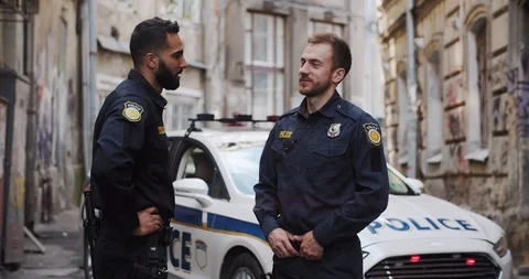Two handsome friendly policemen talking near the police car together patroling Video stock 112953087
