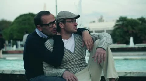 Two handsome men sitting on bench and smiling to the camera, slow motion Stock Footage 12555677