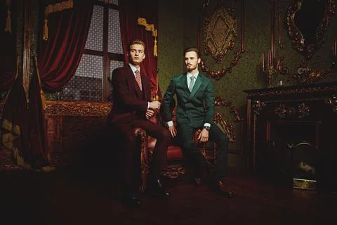 Two handsome young men in elegant classic suits pose in a luxury apartments w Stock Photos
