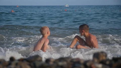 Two happy boys are playing on the seashore with the waves. View from the back. Stock Footage 332758397