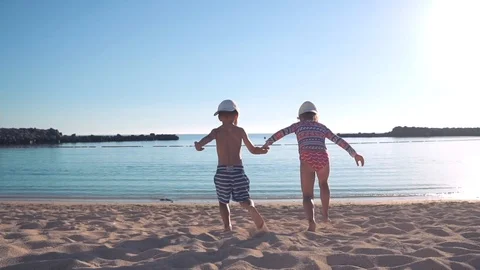 Two happy children, holding hands, run along the sandy beach to the sea and run Stock Footage 101752969