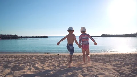 Two happy children, holding hands, run along the sandy beach to the sea and run Stock Footage 101753175