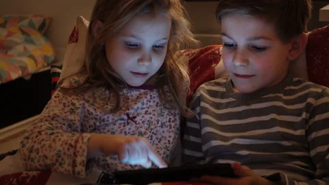 Two happy children playing with tablet in bed Stock Footage 134575853