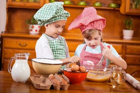Two happy children preparing eggs for cookies in the kitchen Stock Photos