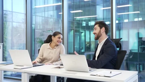 Two happy co-workers communicate casually while working on laptop at desk  Stock Footage 298998051