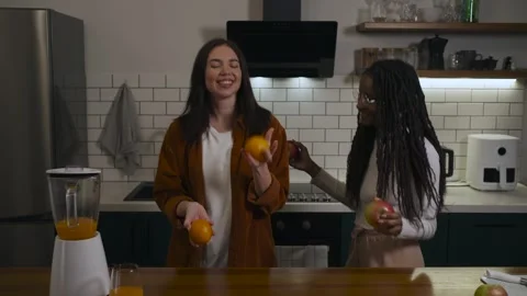 Two happy friends sharing a joyfull moment and dancing with fruits in a kitchen. Video stock 301681683