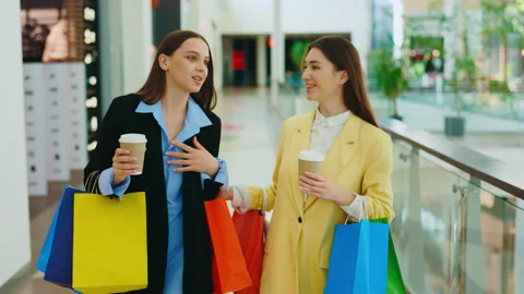 Two happy girlfriends going in the mall after shopping. Woman holding coffee Stock Footage 229323671