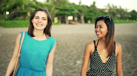 Two happy girlfriends talking walking along beach Stock Footage 53056208