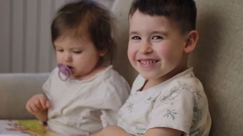 Two happy kids sitting on sofa and reading an interesting book story at home Video stock 202022584