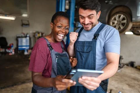 Two happy mechanics cheering while looking at a digital tablet in a garage Stock Photos