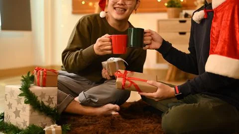Two happy men clinking cups of hot chocolate while celebrating Christmas or New Stock Photos