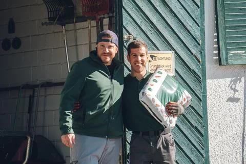 Two happy men collaborating, standing together in a garden shed doorway 库存照片