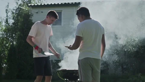 Two happy men cooking grilling bacon and sausages on grid Video stock 143473231