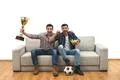 The two happy men with a cup watch a football on the sofa Photo