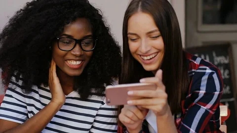 Two happy multi-ethnic friends sitting in cafe and laughing at something on Stock Footage 81834274