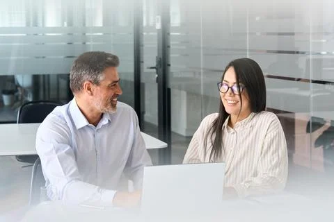 Two happy multicultural professionals working in office using laptop, talking. Stock Photos