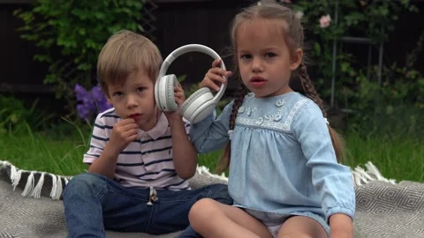Two Happy Siblings boy ans girl listening to music on headphones outside in Stock Footage 198528108