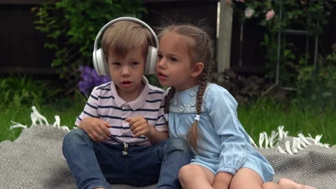 Two Happy Siblings boy ans girl listening to music on headphones outside in Stock Footage 198933986