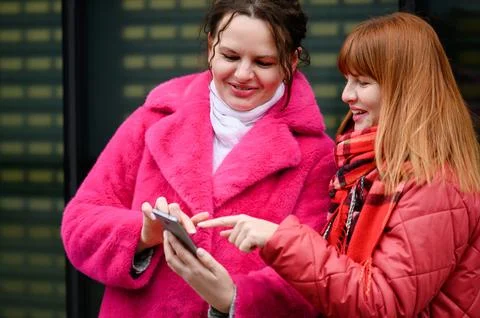 Two happy sisters using smartphone together on city street. Young women in 写真素材