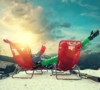 Two happy skiers sitting in chaise-longues on the top of snow mountain Stock Photos