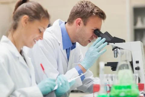 Two happy students looking through microscope and taking notes 스톡 사진