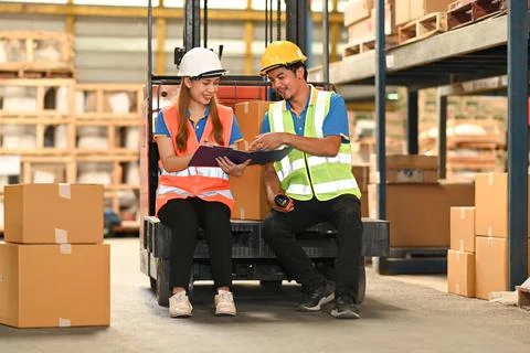 Two happy warehouse worker sitting on forklift truck checks stock and inventory Stockfoto's
