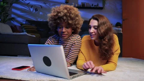 Two happy woman laughing at computer screen lying on the floor. Smiling lesbian Stock Footage 243920102