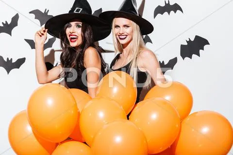 Two happy women in witch halloween costumes with orange balloons Stock Photos