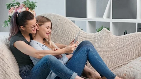 Two happy young charming lesbian girl looking at screen of tablet pc hugging Stock-Footage 116464528