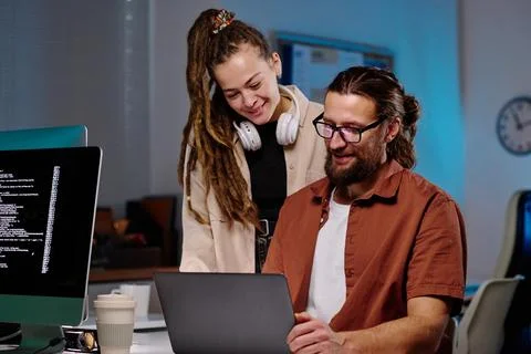 Two happy young programmers looking at laptop screen with coded data Stock Photos