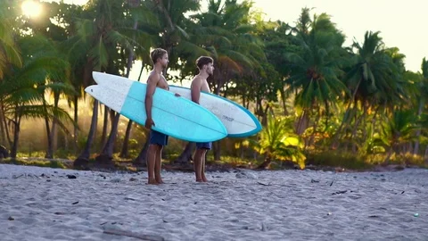 Two happy young surfers friends holding surfboards. beautiful golden sunrise  Stock Footage 108564329