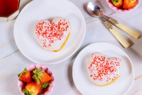 Two heart shaped donuts with white glaze and pink, red sprinkles on a platet  Stock Photos