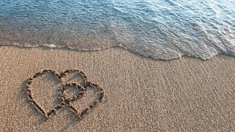 Two hearts drawn on brown sand of paradise beach Stock Photos