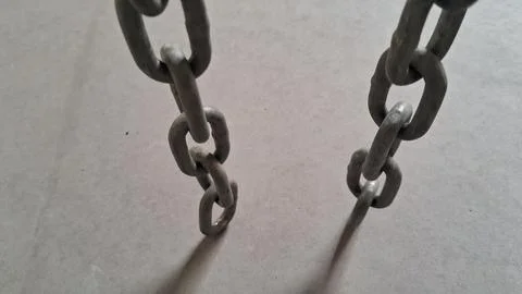 Two heavy metal chains hanging down against a plain grey background Stock Photos