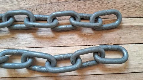 Two heavy metal chains resting on a rustic wooden background surface Stock Photos