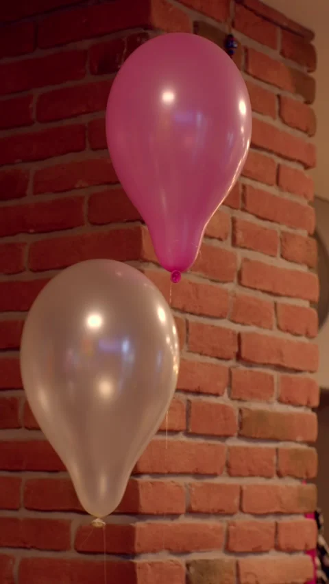 Two helium balloons floating beside a warm red brick column in an interior Vídeos de archivo 336535465