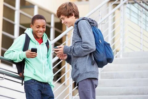 Two high school students outside building with mobiles Fotos de archivo