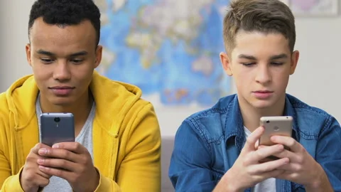 Two high schoolers browsing dating apps on smartphones, choosing girlfriends Stock Footage 103399288