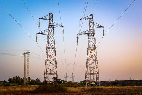 Two high voltage power pylons in a rural field at sunset. Foto stock
