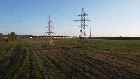 Two high-voltage towers stand in a field against the backdrop of a road filled Video stock 319894733