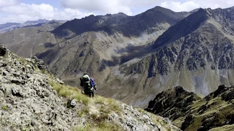 Two hikers are walking through difficult mountainous terrain on a cliff slope Stock Footage 252766028
