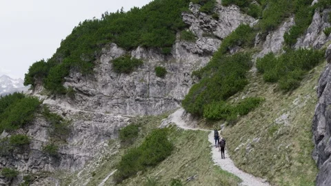 Two hikers with backpacks walking along a winding trail carved into a steep Stock Footage 336942014