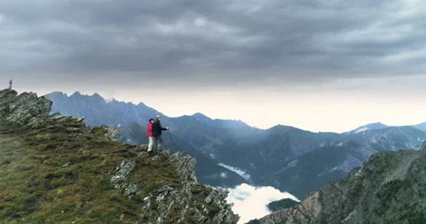Two hikers on the edge of the mountain. Couple Tourists peak of rock. Aerial Stock Footage 107048766