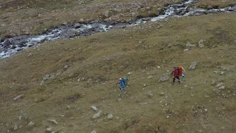 Two hikers with large backpacks walk along a stormy mountain river Stock Footage 259792838